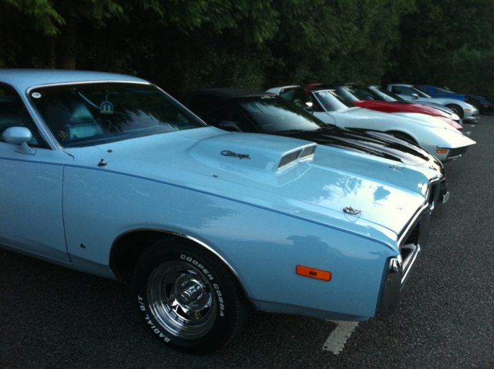 Wednesday Valley Pistonheads Thames Night July - The image captures a serene scene of a parking lot, where ten classic cars are parked neatly in two rows. The cars are a vibrant mix of blue and red, adding a touch of excitement to the otherwise tranquil setting. Each car is distinct, with unique models and designs, but they all share the common feature of a white hardtop convertible top. This uniformity in the top's color contrasts with the variety of the car's bodies, creating a pleasing array of colors against the backdrop of the parking lot. The cars are oriented towards the right side of the frame, suggesting directionality and movement towards an unseen destination.