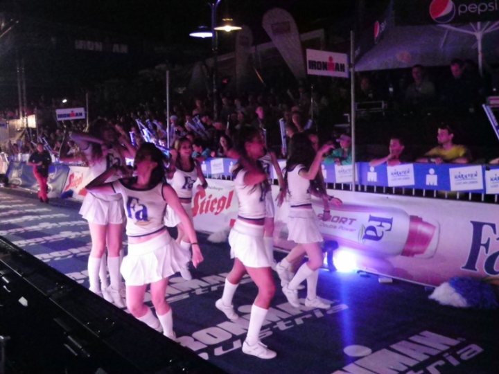 Pistonheads - The image captures a dynamic event at night, featuring a large crowd of people with candles, and three girls dressed predominantly in white. Each girl is on rollerblades, skillfully navigating a track that has 'Iron Man' written on it, along with other text and logos. The crowd appears to be cheering from behind a barrier, engaged in the competitive atmosphere. The predominant colors in the image are dark, highlighting the white outfits of the rollerbladers and the bright lights illuminating the scene.