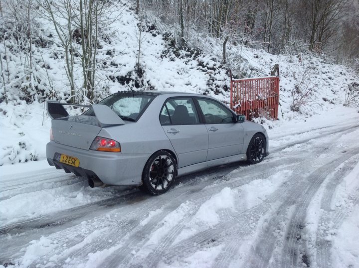 New to the forum,so posting a few pics of my car. - Page 1 - South Wales - PistonHeads - The image features a light gray car with a black rear spoiler and white rims parked in a snowy landscape. The car is partially covered in snow, indicating it has been parked for some time. In the background, there is a wooden fence partially obscured by snow and a red structure. The snow-covered ground suggests the photo was taken during a heavy snowstorm. The sky is not visible in the image, and the focus is on the car and its immediate surroundings.