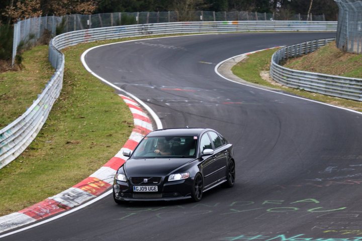 Volvo S40 T5 K16 - Page 1 - Readers' Cars - PistonHeads - The image captures a dynamic scene on a racetrack. A black car is seen navigating the right turn of the track, leaning into the curve with its front facing to the left. The track itself has a tarmac surface and features multiple layers of tires, which are typically used for racing events. 

On either side of the track, there are grassy areas that provide a natural contrast to the paved racing surface. The background is characterized by a clear sky, suggesting favorable weather conditions for outdoor activities like this. Additionally, there is a signage visible in the image, likely providing information or directions related to the racetrack.