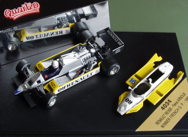 Pistonheads Collection - The image showcases a vibrant display of two toy race cars, both labeled "Final Fantasy." The cars are positioned on a black tray, with one car placed slightly behind the other, suggesting a race scenario. One car is primarily yellow with accents of blue and white, while the other is predominantly white with bold yellow stripes. Above the toy race cars, there's a glass enclosure with a display card inscribed with the text "Renenault G. P. 1986," hinting at the historical relevance of the cars.