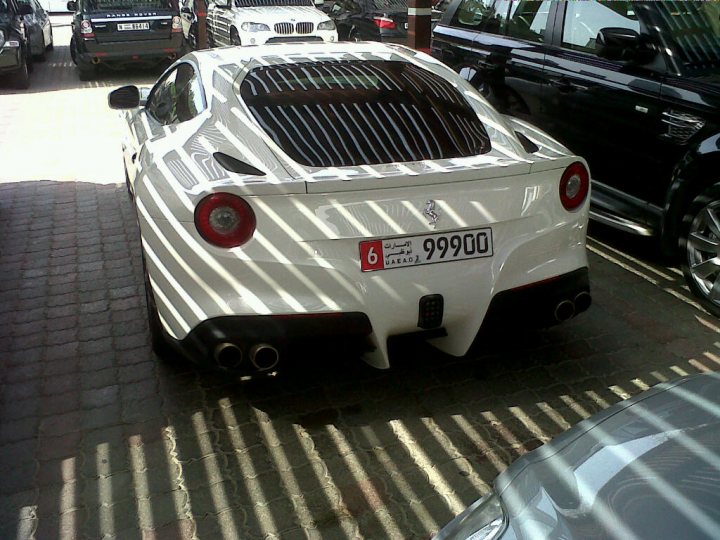 - Page 1 - Supercar General - PistonHeads - The image shows a black and white Ferrari parked in a lot on a sunny day. The car is sleek with its sporty design and prominent red taillights. The front of the car is adorned with a large, rectangular number plate that reads "9990". The surrounding area of the car is lined with other vehicles, including other sports cars and a utility vehicle, indicating the setting might be a luxury car show or retail area.