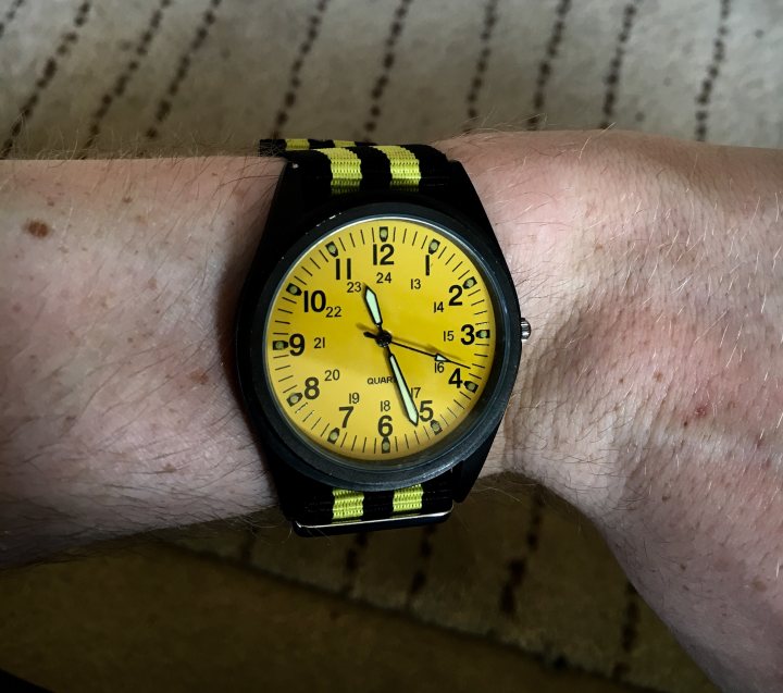 Let's see your NATO's  - Page 12 - Watches - PistonHeads - The image shows a close-up view of a person's wrist, with the watch positioned over a hand's movement. The watch has a vibrant yellow face with black numbers and hands. It features three smaller dials, possibly for additional functions like a stopwatch or chronograph. The band of the watch is black with a yellow stripe along the edge. The overall theme suggests a sporty or casual style, and the wrist on which it sits seems to be in motion, indicating activity.