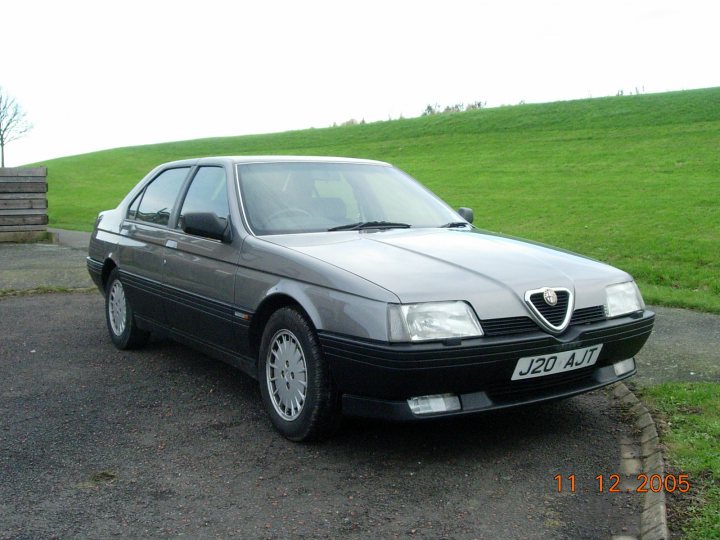 RE: Shed of the Week: Alfa 164 Twin Spark - Page 6 - General Gassing - PistonHeads - The image appears to depict a scene outdoors. There is a car parked on what looks like asphalt near some grass. The car is an older model, with a visible V-badge on the grill, suggesting it may be from the era of the Fiat V10. The date stamp in the bottom right corner, "11.12.2005," indicates the photograph was taken on November 12th, 2005. The surroundings include a dirt patch and what could be an informal or rural setting, with no distinct man-made structures visible in the image. There are no people visible in this picture.