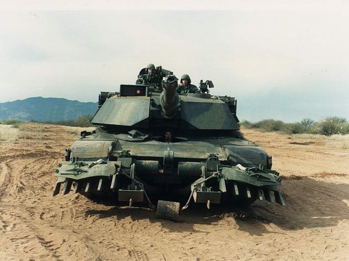 Legal Off Road Modifications - Page 1 - Off Road - PistonHeads - The image depicts a military scene with a large tank sitting on a dirt field with tire tracks visible around it. There are three individuals visible, who appear to be passengers or crew members within the tank. In the background, there are mountains in the distance, suggesting a desert or arid environment. The tank is positioned in a way that it makes an angle to the camera, revealing its treads and turret. The image has an aged or vintage quality, suggesting it might be an old or historical photo.