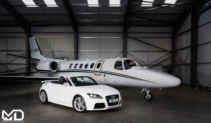 A large white airplane sitting on top of a tarmac - Pistonheads - The image showcases a sophisticated white sports car positioned in front of a private, single-engine aircraft. The car appears sleek and modern, drawing attention with its distinctive design and high-performance status. The airplane, with its blue and white stripes, sits idle with its doors open, waiting for its next journey.

The setting is within a hangar, characterized by its high ceiling and exposed rafters, providing a stark contrast to the glossy, professional appearance of the airplane and sports car. The juxtaposition of the two elements - the high-speed luxury automobile and the personal jet - suggests a blend of opulence and luxury with an emphasis on the ease of travel by private aviation.