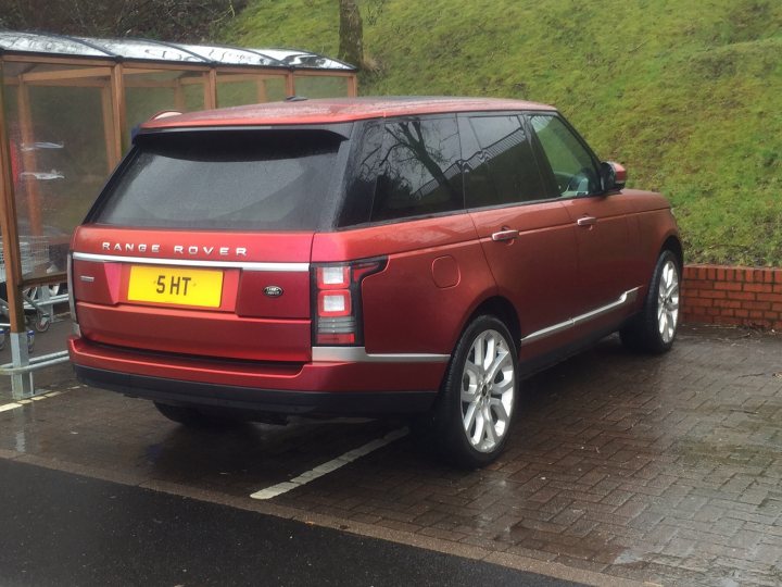 Real Good Number Plates : Vol 4 - Page 299 - General Gassing - PistonHeads - The image showcases a red Range Rover Sport parked on a wet street. The car bears the license plate "5HU". It's positioned in front of a bus stop shelter, which provides some protection against the elements. The backdrop consists of a metal railing and a brick wall, setting an urban outdoor scene. The overall scene suggests it might have rained recently, as indicated by the wet surface of the street.