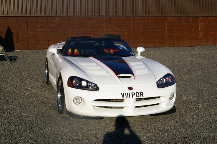 Blown But Not Blown - Page 1 - Vipers - PistonHeads - The image captures a scene featuring a white sports car positioned at an angle, giving a clear view of its bodywork and front licence plate that reads "VILLPOR." This vehicle features a distinctive design with a sleek, low-profile silhouette and a prominent hood scoop. In the background, a person is standing at a distance, providing a sense of scale to the scene. The car is parked on an uneven surface, possibly a gravel or dirt area, next to what seems to be a wooden fence, adding to the rural feel of the setting.