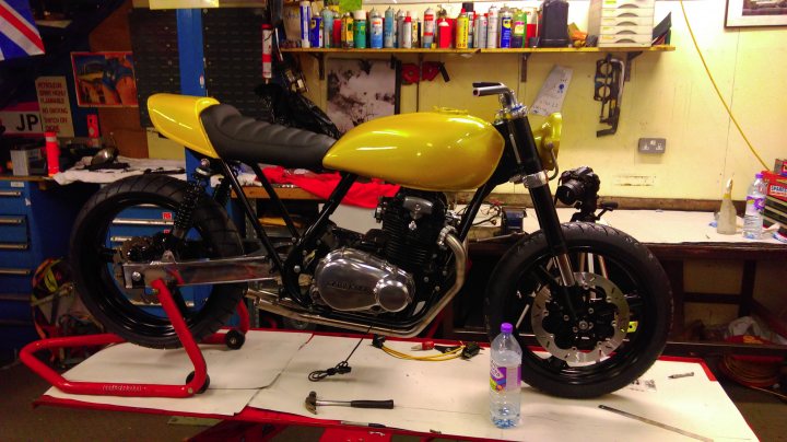 A motorcycle is parked on the side of the road - Pistonheads - The image portrays a custom motorcycle model in a workshop setting. The motorcycle is predominantly yellow with a black seat. It has a unique design with a large engine and round headlights. The motorcycle is mounted on a red stand within the workshop space, which is equipped with various tools and supplies. The background reveals a well-organized workspace with a collection of different objects and pieces of equipment.