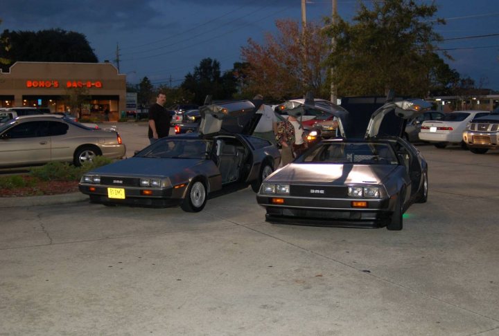 Piston Delorean Heads Pistonheads - The image depicts a parking lot filled with various vehicles, with a focus on a couple of classic cars. There is a man standing near some of the cars, possibly admiring them. Interestingly, one of the cars has its hood open, revealing its engine. The lot is situated in front of a building, possibly a store, under a dark sky, suggesting it might be evening. Overall, the scene captures a moment of urban life with vintage cars being the main attraction.