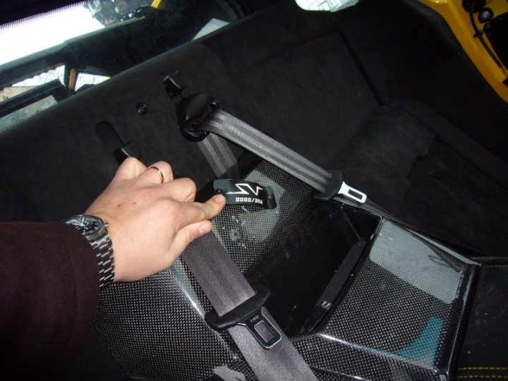 White Lps Pistonheads - The image shows an interior view of a vehicle, focusing on an airbag mat placed in the back of a passenger seat. A hand is seen adjusting the seat belt, which has a gray cover and a black buckle with a "5 Bolt" logo. The cabin is upholstered in a dark fabric, and through the vehicle's rear window, the outdoors appears blurry, suggesting motion.