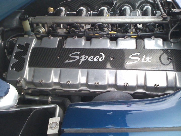 Show us your powder coloured engines - Page 2 - Speed Six Engine - PistonHeads - The image features a close-up view of a vehicle's engine bay, focusing on the intake manifold. The text "Speed 6" is prominently displayed on the engine cover, possibly indicating a performance enhancement for the vehicle. The engine cover appears to be painted or coated in black, which contrasts with the metallic engine parts beneath it. The engine itself has various hoses and components, suggesting a complex and powerful mechanism. The visible portion of the vehicle suggests a deep, vibrant blue color scheme, which, combined with the potential for further tuning, could imply a performance-oriented vehicle.