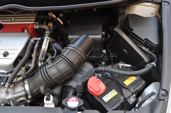 Pistonheads Type Import - The image provides a close-up view of the engine bay of a vehicle, revealing various mechanical components. There is a dark plastic container, possibly an air filter box, located near the gas tank. A black hose is visible, running parallel to a smaller black hose. A large curved tube or pipe is prominently positioned in the center, with an end visible on the left side of the image. The engine appears to be a V8 type, indicated by the different compartments and the number of cylinders implied by their arrangement. The image captures the complexity and intricacy of an internal combustion engine.