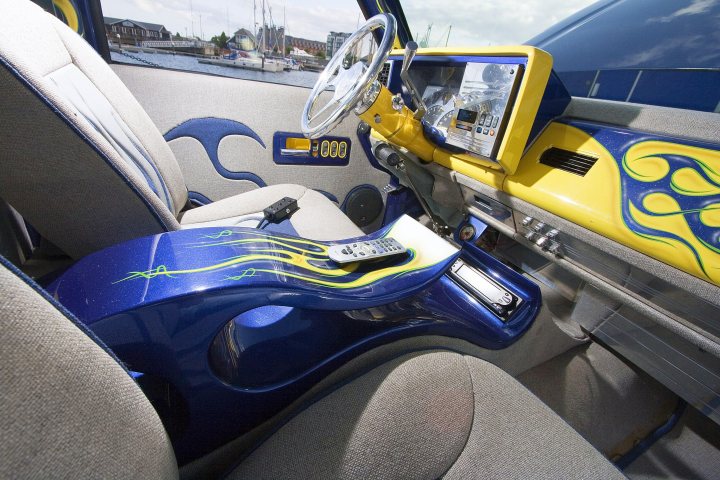 Pistonheads Truck Chevy - The image features the interior of a vehicle, specifically the cockpit area. The main focus is on a blue and yellow flaming guitar that has been creatively integrated as the center console of the vehicle. The guitar's design includes painted flames and musical notes, and the neck of the guitar has been transformed into the gear shifter. Inside the gear shifter, there's a remote control inserted. The vehicle appears to be a convertible, suggesting a relaxed and leisurely driving experience. The cat's eye, which is part of the steering wheel, can be seen in the background, adding to the unique and personalized design theme of the car.