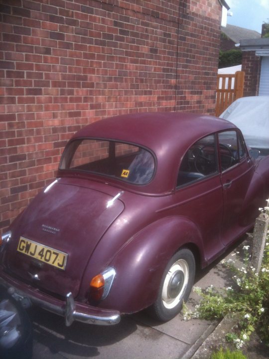 1971 Morris Minor 1000 Resto thread (Maybe) - Page 1 - Classic Cars and Yesterday's Heroes - PistonHeads - The image depicts an old, red Volkswagen Beetle parked in a driveway. The car has a white icing streak on the hood, suggesting it was once white. The license plate reads "GWJ 407J". Behind the car, there's a brick wall and a wooden fence, adding to the traditional, residential feel of the scene. The sky in the background gives a clear, daylight setting to the image.