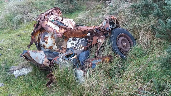 Classics left to die/rotting pics - Vol 2 - Page 74 - Classic Cars and Yesterday's Heroes - PistonHeads - The image shows a severely damaged motorcycle that has been abandoned or is awaiting repairs. The motorcycle is lying on its side, with its engine exposed and the paintwork significantly worn out. It appears to be situated in a grassy area that suggests a field or pasture, with some trees visible in the background. The rot and rust on the motorcycle indicate that it has been exposed to the elements for quite some time. The image conveys a sense of abandonment and potential recycling value.