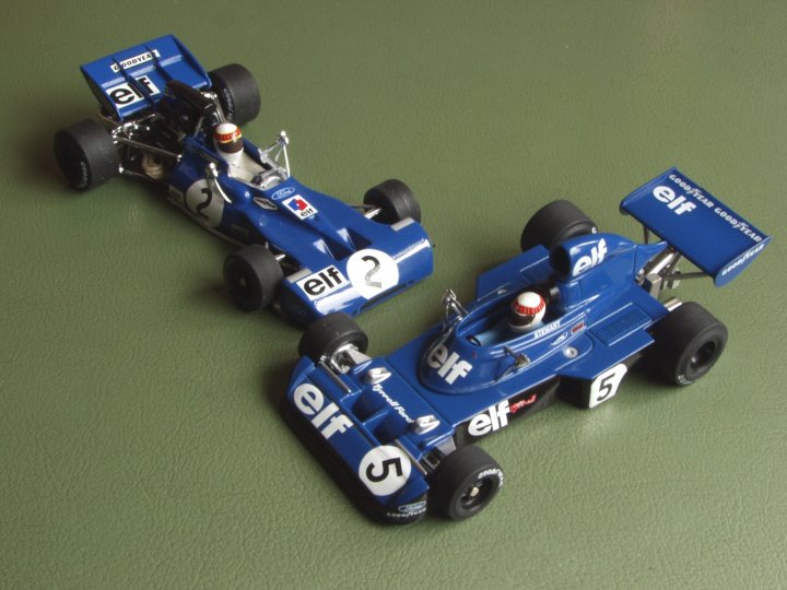 Collection Pistonheads - The image shows two toy diecast racing cars positioned side by side on a flat surface, which appears to be a green tabletop. Each car has blue and white livery with "ELF" printed on the sides, indicative of theELF office equipment company's association with Formula 1. The cars are positioned facing the viewer, and the white color of the "ELF" lettering contrasts with the darker blue and black of the model cars. The setting and arrangement suggest these models might be collectibles or part of a miniature racing display.