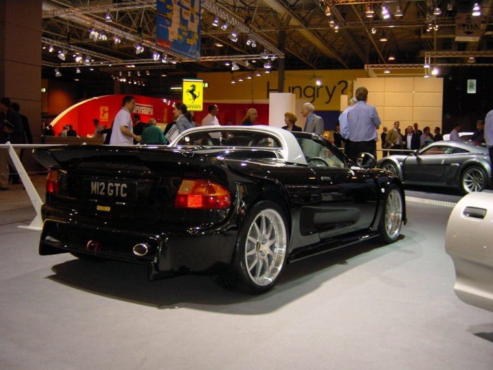 A car that is sitting in the street - Pistonheads - The image captures a sophisticated setting inside a large exhibition hall or museum. Dominating the scene is a sleek, black sports car with a convertible top, proudly on display for viewers. The car's design implies speed and style, suggesting it may be a sports or luxury vehicle.

Other people can be observed in the background, examining various objects or vehicles on display. This gathering indicates that the car may be showcased for an event like a motor show or a car exhibition.

The hall itself is spacious and well-lit, with high ceilings and structural columns. This architectural style allows for plenty of natural and artificial lighting, enhancing the visual appeal of the exhibited items. 

To the side of the car, you can see another vehicle, although details about this particular car are not clearly visible. The red and white color scheme suggests that there might be multiple cars displayed in the same area.

Please note that this description is based on the known information within the image and should not be considered as facts. It is an interpretation based on the visual content provided.