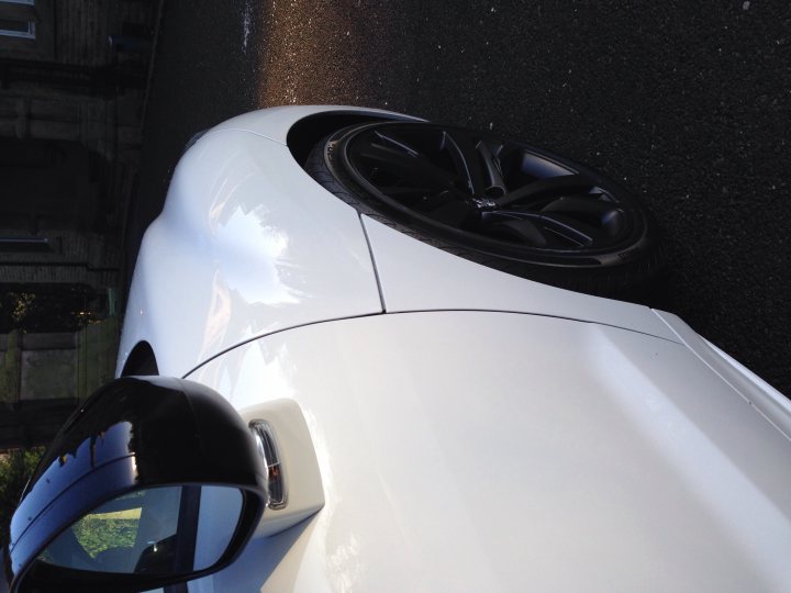 Magic Detail Altrincham - Page 1 - North West - PistonHeads - The image displays a close-up view of a white sports car. The focus is on the front fender and tire, showcasing the car's distinctive aerodynamic design. The tire is a vibrant black, sharply contrasting against the silver rims and the smooth surface of the car's fender. The tires' glossy finish reflects some of the surrounding environment, adding depth to the image. The lighting casts interesting shadows, highlighting the contours and curves of the car's design.