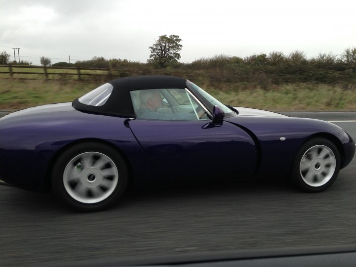 A classic car parked in a parking lot - Pistonheads - The image depicts a man driving a purple sports car. The car features a distinctive bubble top and a removable front screen. The scene captures the car on a roadway, suggesting motion. No other vehicles or identifiable landmarks are discernible in the background. The overall impression is of a classic or vintage sports car being driven by an individual.