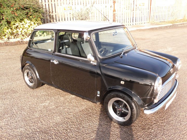 Sell or keep, MOT or don't? - Page 1 - Classic Minis - PistonHeads - The image showcases an antique black Mini Cooper car parked on a dirt lot with a picket fence in the background. The car appears to be well-maintained, with a shiny exterior that reflects the surrounding area. The white-topped interior is contrasted by the black exterior, contributing to the overall compact design of the car. The presence of the logo on the hood and the distinctive design elements suggest that this is a Mini Cooper. The image captures the charm and nostalgia associated with vintage vehicles.