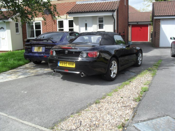 S2k. Vs Boxter s - Page 1 - Honda - PistonHeads - The image shows the rear view of a black Honda sports car parked in a driveway alongside a row of white-finished homes. The car has a British-style license plate that reads "Y58 HK". The setting seems to be a residential area with neatly maintained front lawns. The sky is overcast, suggesting an overcast day.