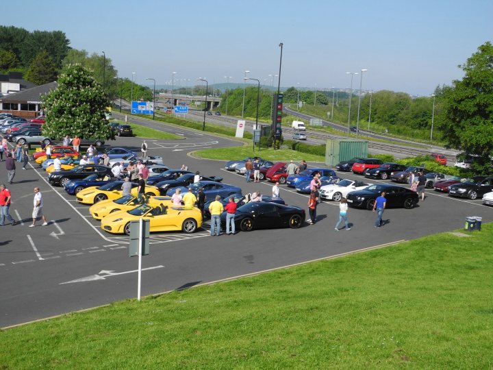 Gordano this morning en route to cwc - Page 1 - South West - PistonHeads - The image is a vibrant panorama of a parking lot filled with a variety of cars. The lot appears to be quite large, with multiple rows of vehicles. The atmosphere is lively, with people scattered throughout the scene, some strolling leisurely around the cars, others standing in close proximity, possibly in conversation or admiring the display.

The cars themselves vary significantly in model, color, and size, contributing to a colorful and diverse grouping that catches the viewer's attention. The surroundings suggest that this could be a popular destination, possibly an outdoor auto show or exhibition, given the number and variety of vehicles.

Tall poles with lamps can be seen in the background, indicating the lot's placement near a street or roadway. The overall scene exudes a sense of community and shared interest in cars.