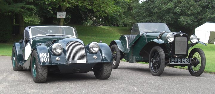 A black and white photo of an old truck - Pistonheads - The image depicts a tranquil scene of an open road with two vintage vehicles parked side by side. The cars are classic models, with the first one to the left featuring an elegant design in green and black. The second car on the right is black and appears to have a larger size compared to the first. They are parked on the shoulder of the road, which is flanked by lush green trees and grass, suggesting a peaceful, rural setting. The weather appears clear, with ample sunlight illuminating the scene, casting soft shadows on the vehicles and the surrounding greenery.