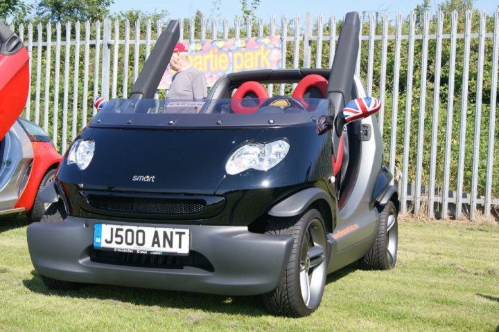 A classic car is parked in a field - Pistonheads - The image showcases a unique black sports car, infused with a touch of British charm, which is registered under the license plate "J500ANT". The vehicle, equipped with two prominent antennas on the roof, is parked in a lot filled with other vehicles. The lot is contained within a metal fence, and the car's vibrant color stands out in the setting.