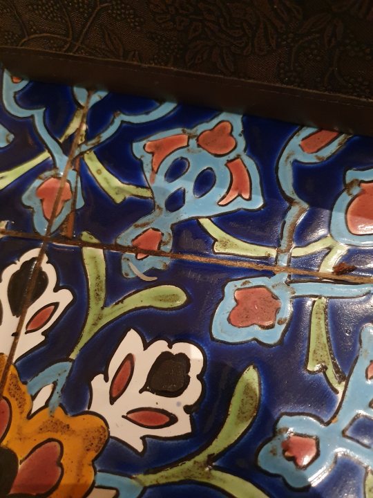 Life has been draining lately... - Page 160 - The Lounge - PistonHeads UK - This image features a close-up view of an ornate, colorful tile table top. The tiles are intricately designed with floral patterns and shades of blue and red. The design includes various shapes and motifs that give it a decorative appearance. The tiles have a textured surface, indicating they might be made from clay or another porous material. There is a visible crack in the tilework, suggesting age or wear. In the background, there appears to be a piece of wood, possibly part of the table structure, which complements the colorful and detailed tiling. The overall image has an artistic and rustic quality to it.