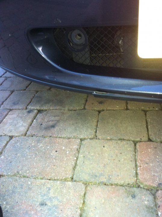 Bumper Amv Front Pistonheads - The image shows the front bumper of a car, which is missing several parts, including parts of the front grille and the emblem, revealing chipped paint and exposed metal. The car is parked on a brick pavement. There are a few loose bricks scattered on the ground around the vehicle. The close-up view highlights the wear and tear on the bumper area, suggesting the car has been in several accidents or has had a long and rough life.