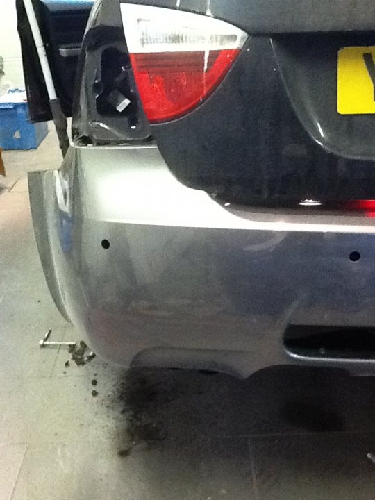 A car is parked next to a parking meter - Pistonheads - The image shows the back of a car in a garage with a concrete floor. The car is a dark color, possibly black or deep blue, with a tinted rear window. The license plate is a distinction with a yellow border and black characters, reading "Y." The photo is taken from an angle that focuses on the rear bumper, slightly tilting upward as you follow the curve of the bumper. The car appears to be a typical sedan, and there is a visible tail light and a fuel flap.