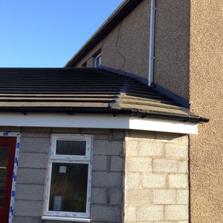 How to seal a pitched roof against the original pebble dash? - Page 3 - Homes, Gardens and DIY - PistonHeads - The image shows a small house with a light brown tiled roof. The roof contains multiple black slates, indicating a combination of different materials.