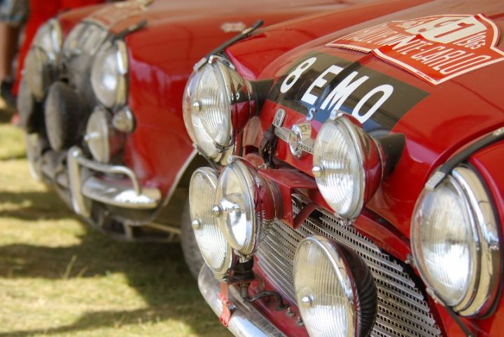 FOS good photography vantage points.. - Page 1 - Goodwood Events - PistonHeads - This image captures a trio of sleek, vintage red cars parked closely together. The front grilles of the cars are adorned with bright, glossy headlights, and the one on the right prominently displays the words "B-EMO" and "CUSTOM GRANDE" in a unique design. The cars are parked on a grassy field, suggesting a setting that might be related to a car show or exhibition. The curved design of the headlights and the overall vintage appearance of the vehicles hint at a classic or retro aesthetic.