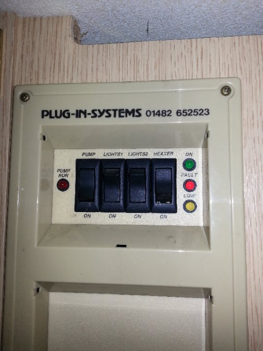 A close up of a nintendo wii game system - Pistonheads - The image shows an electrical device with a beige casing, featuring a digital display on the upper part and a number of control buttons and switches along the bottom. The device appears to be a power control unit, possibly for energy systems, as indicated by the text "Plug-in-Systems". A red light is seen illuminated, and the model number "01482 652532" is visible on the upper left corner. The control buttons are likely for trigering different functions of the system, but their precise functions are not indicated within the image. The device is mounted on a wall with a wooden textured finish, suggesting an indoor setting.