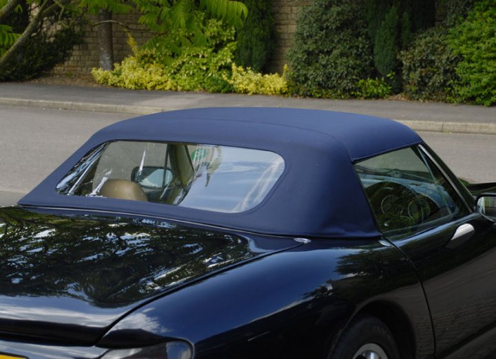 New roof - Rectangle Window (no curve) - Page 1 - Chimaera - PistonHeads - The image shows a black car with a dark blue cover, parked on the sidewalk. It appears to be a classic or vintage model. The cover extends over the rear window, providing shelter and a sleek appearance. The car is parked near a brick building with greenery. The photo seems to have been taken during the day under overcast or cloudy skies.