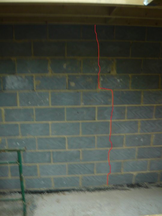 New extension: Internal Cracks - Page 1 - Homes, Gardens and DIY - PistonHeads - The image depicts a wall made of gray bricks with a long, twisted, red line running along its length. The wall appears to be in a corner with one of its edges being a concrete floor. A green metal object, possibly a handrail, is visible on the left side, attached to the wall at the concrete floor level. The image is slightly blurry, making it difficult to discern the precise details.