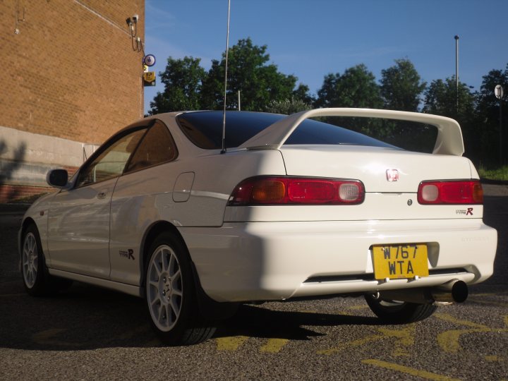 Pistonheads - The image captures a sleek, white two-door Honda, the top of which is adorned with an air spoiler. The car is parked outdoors, with a brick wall serving as a backdrop, enhancing the urban setting. The tail light, marked with the registration "W76WTA" and a Honda emblem, stands out on the trunk. The sunlight casts a shadow on the road, suggesting the photo was taken during the day.