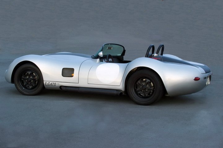 Lucra LC470 - Anyone driven one on here? - Page 1 - Yank Motors - PistonHeads - The image depicts a one-of-a-kind car with a sleek and elongated design. The car features a white, body-like structure, akin to a jet or a teardrop-shaped vehicle. The curved hood and pointed nose are distinctive characteristics of this unique car. On the side, there are markings with numbers, possibly indicating its age or registration details. The car rests on a plain, grey surface, drawing all attention to its futuristic design and contrasting colors.