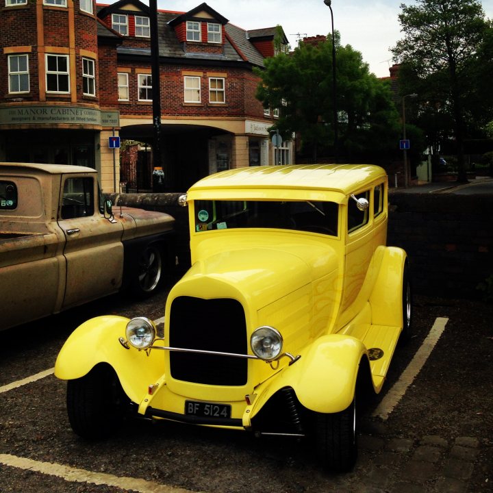 COOL CLASSIC CAR SPOTTERS POST!!! Vol 2 - Page 36 - Classic Cars and Yesterday's Heroes - PistonHeads - The image features a street scene with an eye-catching, bright yellow vintage car parked on the side. This classic vehicle, likely an older model of a sedan or station wagon, is clean and shiny, suggesting maintenance and care. The car is significantly larger than the other vehicles present in the image. In the background, there is a building with an architectural design that suggests it might be located in an older area of a town. There are also traffic lights and street signs, contributing to the urban setting. The overall scene conveys a nostalgic and peaceful atmosphere.