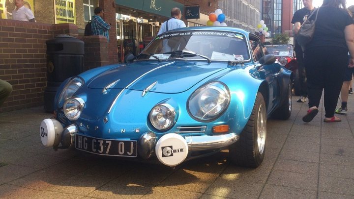 Camberley Town Centre car show - Page 1 - Thames Valley & Surrey - PistonHeads - The image showcases a small blue vintage car as the main focus, parked on a shaded sidewalk next to a brick wall. Behind the car, there are people and other vehicles, indicating a street scene. The car's license plate is clearly visible and reveals a French registration, reading "G36 OJ". A few individuals are standing close to the car, suggesting interest or admiration for the vehicle. The overall atmosphere of the image is casual and leisurely, with no indicated sense of urgency or immediacy.