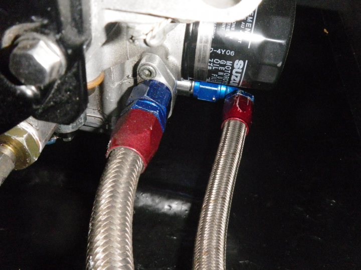 Clubsport ZZR 1100 help - Page 1 - Radical - PistonHeads - The image provides a close-up view of two hoses, each attached to a ring at their ends. The hose in the foreground has a white coating, while the one in the background is red and blue. Both hoses are connected together by a metal ring, which serves as a fitting, and they are situated in a dark, possibly industrial, background. There are texts visible on the fittings, though they may not be legible in this image. The image is a bit blurry, making details slightly hard to discern.