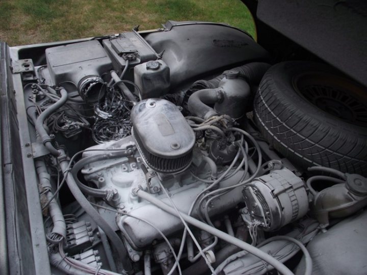 A black and white photo of a motorcycle - Pistonheads - The image shows an open hood of a vehicle, where the engine and exhaust system are visible. The engine appears to be old and dirty, indicating potential wear and neglect. The exhaust pipe can be seen on the left side of the photo, with the engine lying above it. Tangled wires and various engine parts are evident, highlighting the complexity of car mechanics. The grassy area and the spare tire in the background suggest the photo might have been taken outdoors, possibly before or after a repair or maintenance task.