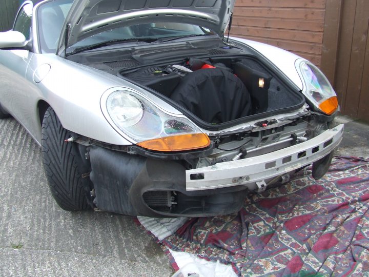 Aircon Broken Pistonheads Cayman Leaking - The image depicts a compact sports car with its hood raised, revealing the intricate details of the engine compartment. The vehicle is white and appears to be a soft-top convertible. It's parked on a surface with a black tarp beneath it. The car owner is reaching under the hood, possibly seeking to fix a problem or replace a component. The car's hood appears to be slightly cracked, but the engine itself is not clearly visible due to the hood being propped up.