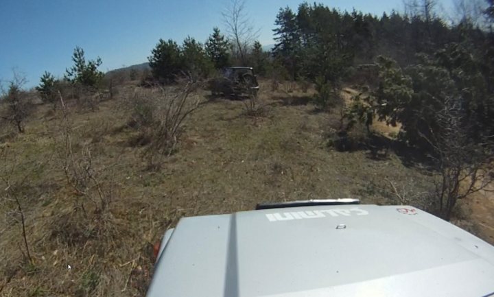 Bit of off-roading, and a bit of camping. - Page 1 - Off Road - PistonHeads - The image shows a scene from a sports utility vehicle (SUV) equipped with an ATV (All-Terrain Vehicle). The vehicle is on a dirt road, with its rear-facing tire visible. The terrain around the vehicle appears rough, with several dead or bare trees, suggesting a change in seasons or perhaps a less cultivated or maintained area. The sky is not visible, but the overall tone of the photo is daylight with natural lighting, which casts shadows on the ground. The purpose or the brand of the ATV is not clearly visible.