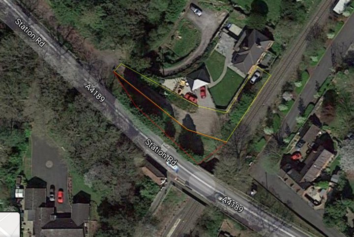 Who owns this (publicly owned) land? - Page 1 - Homes, Gardens and DIY - PistonHeads - The image displays an aerial view of a residential area. There is a distinct, outlined shape on the ground that appears to be a property boundary or some form of demarcation. Adjacent to this marked area is another property with a red roof, indicating different ownership or usage. The surrounding environment includes green spaces, possibly parks or gardens, and roads leading to it. The sky is overcast, suggesting a cloudy day. The overall scene depicts a quiet neighborhood with various types of structures.