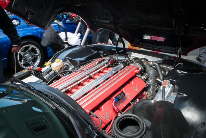 A group of motorcycles parked next to each other - Pistonheads - The image showcases the power of a black muscle car. The car's hood is open, revealing its massive red engine with several tubes extending from it. The engine appears to be a V8, as indicated by the visible six-cylinder structure. The scene also includes a blue car and a person standing to the left of the frame. Lastly, there is a gasoline tank visible in the background. This image captures the mechanical complexity and impressive design of high-performance cars.