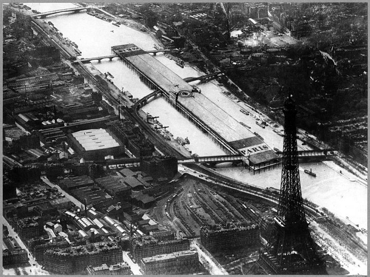 Post amazingly cool pictures of aircraft (Volume 2) - Page 444 - Boats, Planes & Trains - PistonHeads - The image is a black and white photograph showcasing an urban scene. It features a river with a bridge in the distance, flanked by buildings on either side of the waterway. A large industrial area can be seen in the background, with numerous cranes and structures indicative of a bustling industrial setting. The river appears to be calm and wide, and the bridge seems sturdy and well-constructed. In the foreground, there is a partial view of what seems to be a railway line or an overpass leading into the distance. The watermark in the bottom right corner suggests that this image may have been sourced from the internet.