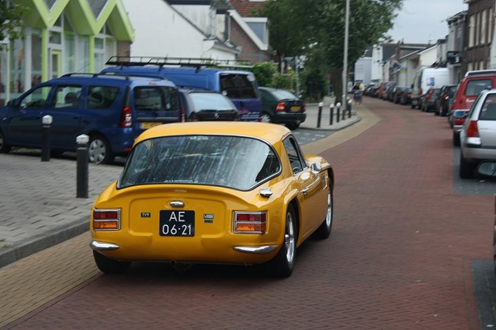 Early TVR Pictures - Page 81 - Classics - PistonHeads - In the image, a vibrant yellow AE11 06172 vintage car is driving down a narrow cobblestone street with parked cars on both sides. The setting appears to be a small town or a part of a city with provincial charm. Various other cars are parked along the street, highlighting the narrowness of the road. The vintage car stands out, possibly indicating a special event or a celebration of historic automobiles.