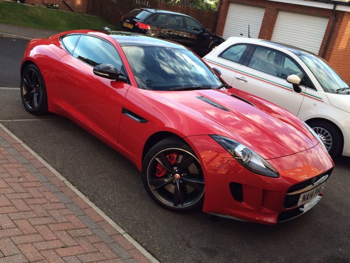 Whats the best colour for a F-type coupe - Page 1 - Jaguar - PistonHeads - This is a photograph of a red two-door luxury sports car parked in a residential driveway. The car has striking red accents and a sleek coupe design. It has black rims on its black tires, and the vehicle appears to be in excellent condition. The driveway is constructed of paving stones, and there are other cars parked behind the sports car. The overall scene conveys a sense of luxury and prestige.